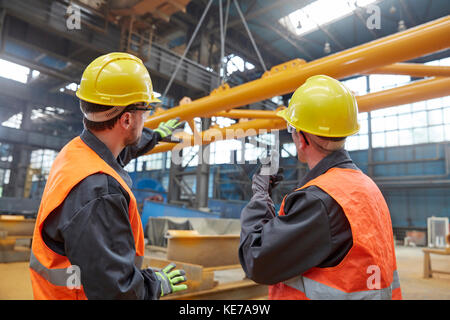 Lavoratori di sesso maschile che guardano le attrezzature che vengono sollevate in fabbrica Foto Stock