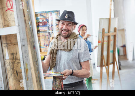 Ritratto sorridente artista maschile pittura a easel in classe d'arte studio Foto Stock