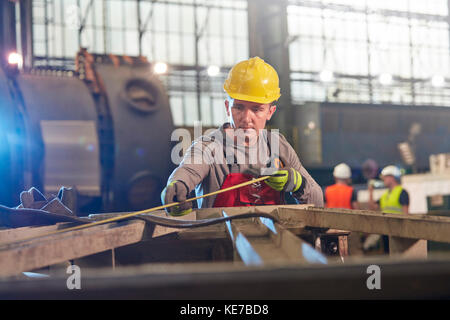 Lavoratore maschile con metro a nastro in acciaio in fabbrica Foto Stock