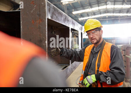 Lavoratore maschile gesturing, spiegando parte in acciaio al collega in fabbrica Foto Stock