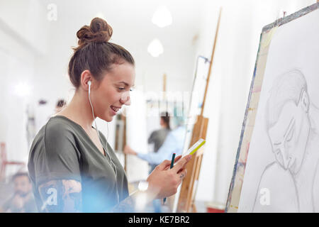 Sorridente artista femminile con cuffie che ascoltano musica e schizzi in studio d'arte Foto Stock