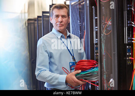 Ritratto tecnico IT di sesso maschile che tiene i cavi nella sala server Foto Stock