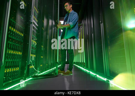 Tecnico IT maschile che lavora in una stanza server buia con illuminazione pannelli verdi Foto Stock