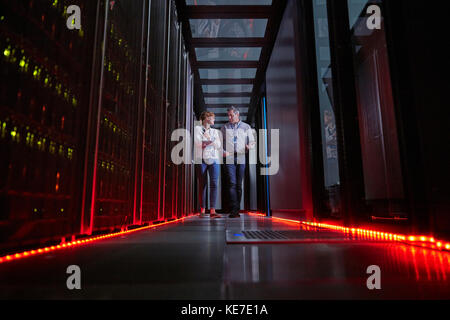 I tecnici IT parlano e camminano nella stanza dei server buia Foto Stock