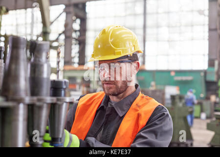 Lavoratore maschile focalizzato che esamina parti in acciaio in fabbrica Foto Stock