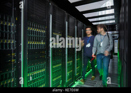 I tecnici IT camminano e parlano in una stanza server buia Foto Stock