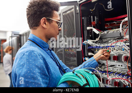 Tecnico IT maschio che collega il cavo al pannello nella sala server Foto Stock