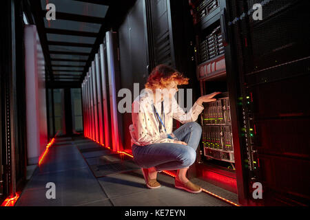 Tecnico IT femminile che esamina il pannello in una sala server buia Foto Stock