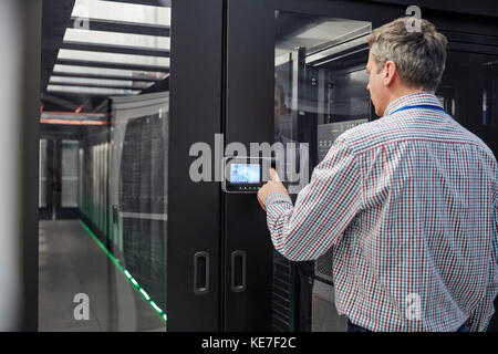 Tecnico IT maschile che ha inserito il codice di sicurezza all'accesso alla sala server porta Foto Stock