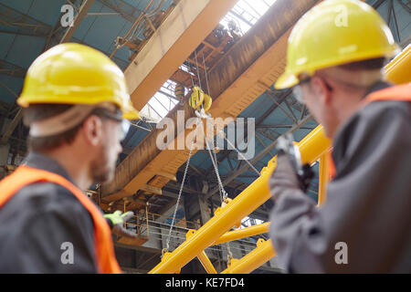 Lavoratore maschile che utilizza walkie-talkie per guidare l'attrezzatura di abbassamento della gru idraulica in fabbrica Foto Stock