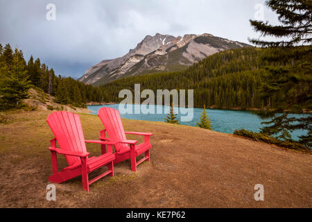 Due Red Adirondack sedie su una collina erbosa in Alberta's montagne e laghi; Alberta, Canada Foto Stock