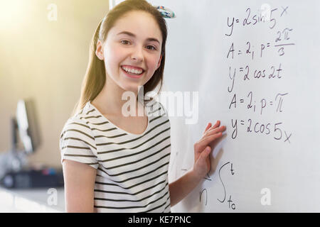 Ritratto sorridente, studentessa sicura risolvendo l'equazione fisica alla lavagna in classe Foto Stock