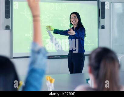 Sorridente insegnante di scienze che conduce la lezione alla proiezione schermo in in aula Foto Stock