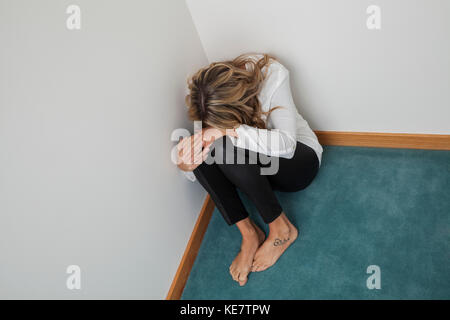 Giovane donna con capelli lunghi biondi seduto in un angolo della stanza con la testa in giù; Connecticut, Stati Uniti d'America Foto Stock