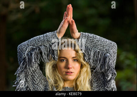 Bambina guarda direttamente nella fotocamera, tenendo le braccia sopra la sua testa, dorso delle mani insieme, in una posa testa e spalle. Foto Stock