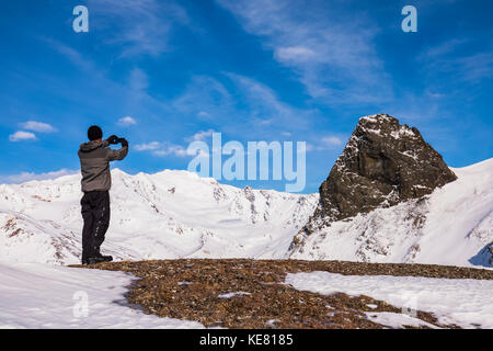 Un uomo su una cresta nell'orientale Alaska Range scatta una foto di una grande roccia affiorante in inverno; Alaska, Stati Uniti d'America Foto Stock