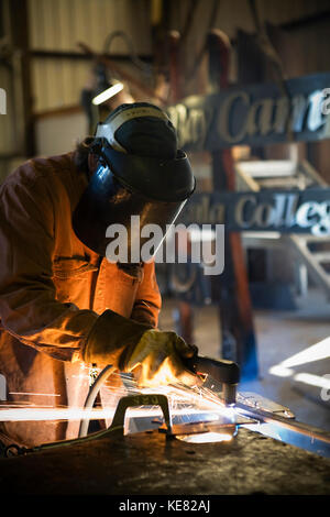 Saldatore e lavoro di metallo artista Doug Schwiesow lavorando su un segno personalizzato progettato con un artista locale per la Penisola di Kenai College Kachemak Bay Campus. Foto Stock