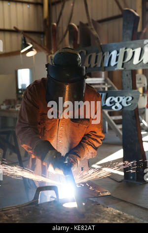 Saldatore e lavoro di metallo artista Doug Schwiesow lavorando su un segno personalizzato progettato con un artista locale per la Penisola di Kenai College Kachemak Bay Campus. Foto Stock