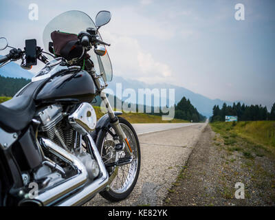 Un motociclo parcheggiato su un lato di un'autostrada con una vista delle montagne in distanza; Spillmacheen, British Columbia, Canada Foto Stock