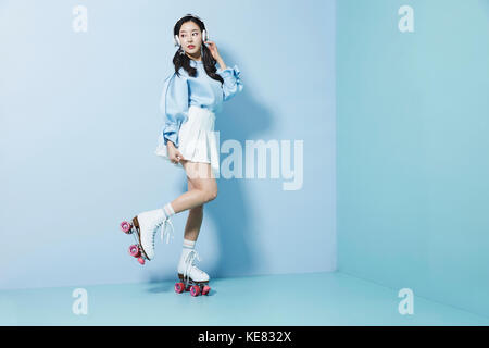 Giovane donna che indossa i pattini a rotelle e le cuffie in posa su un piede Foto Stock