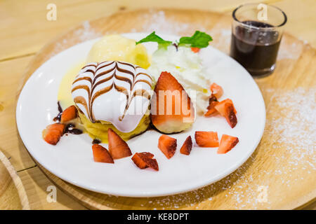 Deliziosi pancake con fragole e gelato alla vaniglia con topping di cioccolato e panna montata su sfondo di legno Foto Stock