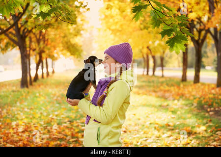 Sorridente ragazza adolescente rilassante con il cane.ragazza che gioca con un piccolo cane all'aperto in autunno Foto Stock