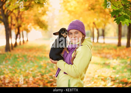 Sorridente ragazza adolescente rilassante con il cane.ragazza che gioca con un piccolo cane all'aperto in autunno. Foto Stock