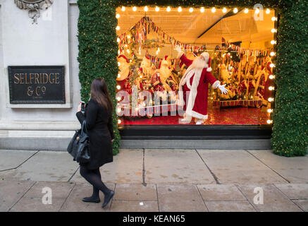 Un attore vestito da padre Natale all'interno di una vetrina di Natale, a tema come con amore da, che è una celebrazione delle città Selfridges chiama a casa, presso il grande magazzino Selfridges a Oxford Street, Londra. Foto Stock