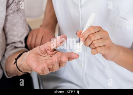 Close-up di medico tenendo dito del paziente controllando il livello di zucchero con il glucometro Foto Stock