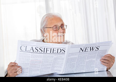 Felice Senior donna quotidiano di lettura sulla scrivania a casa Foto Stock