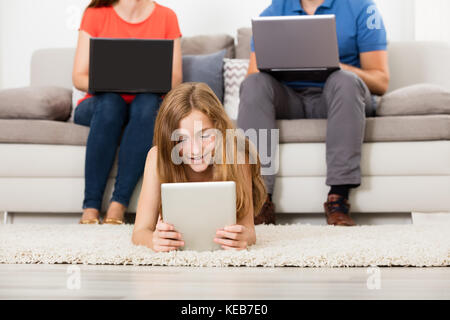 Felice Ragazza con tavoletta digitale nella parte anteriore del suo Genitore lavorando sul computer portatile Foto Stock