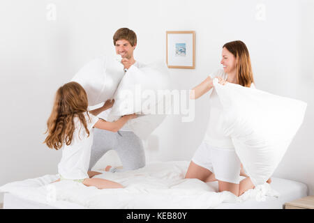 La famiglia felice di lotta di cuscini sul letto matrimoniale in camera da letto Foto Stock