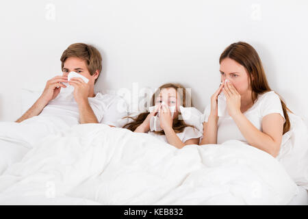 Famiglia giacente sul letto soffia il naso Foto Stock