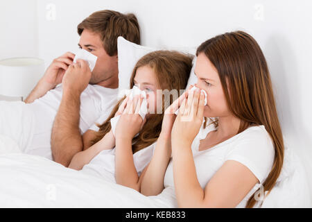 Famiglia giacente sul letto soffia il naso Foto Stock