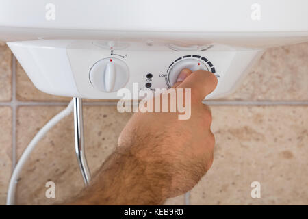 Close-up delle mani dell'uomo ruotando la manopola del boiler elettrico Foto Stock