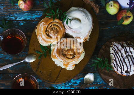 Freschi di forno rotoli alla cannella con la glassa, mele e tè sullo sfondo squallido. vista dall'alto Foto Stock