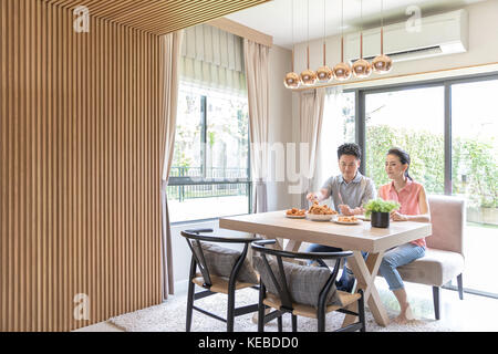 Giovani coppie asiatiche mangiare pollo fritto insieme nel salotto di casa contemporanea per lo stile di vita moderno concetto Foto Stock