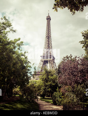 Torre Eiffel, Parigi, in un parco circondato da alberi in primo piano, impostare contro un cielo nuvoloso. Trasformati in un retrò, vintage, stile, inquadratura verticale. Foto Stock