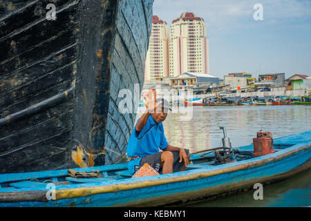 Jakarta, Indonesia - 3 marzo, 2017: la piccola barca blu con locale felice pescatore seduta all'interno, passando dal davanti della barca più grande Foto Stock