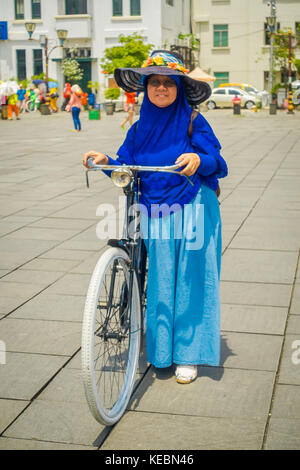 Jakarta, Indonesia - 3 marzo, 2017: donna locale indossando il tradizionale abito indonesiano in posa per fotocamera su city plaza, tenendo le sue bicycke Foto Stock