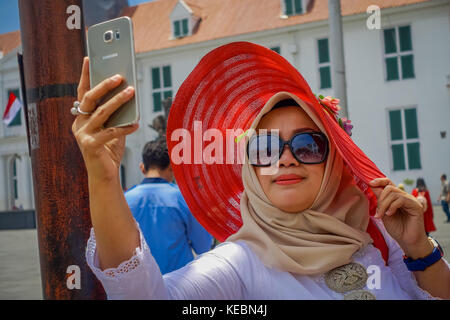 Jakarta, Indonesia - 3 marzo, 2017: donna locale indossando grande Red Hat prende un selfie mentre posa con occhiali da sole Foto Stock