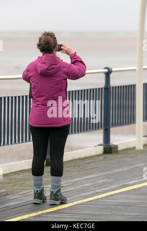 Southport, Merseyside. Regno Unito Meteo. 20 ottobre, 2017. Grigio, umido, blustery per iniziare la giornata al litorale. Giornata di ottobre in acque basse con cieli grigi e venti prevalenti come i residenti locali, le famiglie e gli individui di prendere leggeri esercizi sul molo di resort e il lungomare. Ulteriori bagnato e ventoso è previsto per le zone costiere con gales probabile. Credito: MediaWorldImages/Alamy Live News Foto Stock