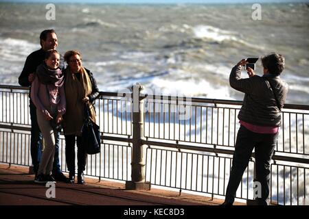 Hastings, East Sussex, Regno Unito. Xx Ottobre 2017. Soleggiato con molto blustery condizioni, la velocità del vento di 25mph e raffiche di vento fino a 41 km/h. Questi turisti sembrano non mente anche se come un membro della famiglia prende una foto su un telefono cellulare. Previsioni per maltempo per il fine settimana. Photo credit: Paolo Lawrenson /Alamy Live News Foto Stock