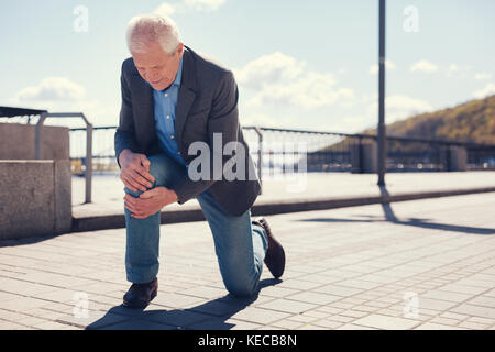 Ben vestito uomo senior sensazione il suo ginocchio dopo la caduta Foto Stock