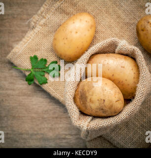 Primo piano freschi Patate organico nella canapa amore borsa con prezzemolo su tavola in legno rustico preparazione per la cottura. messa a fuoco selettiva la profondità di campo. Foto Stock