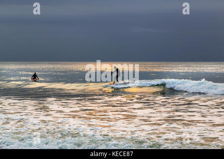 Surf vicino al molo di Bournemouth con il RISING SUN colata di un bagliore giallo sull'acqua Foto Stock