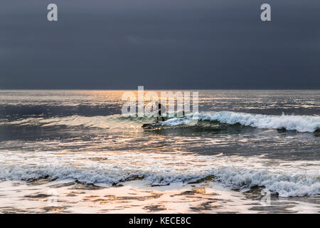 Surf vicino al molo di Bournemouth con il RISING SUN colata di un bagliore giallo sull'acqua Foto Stock