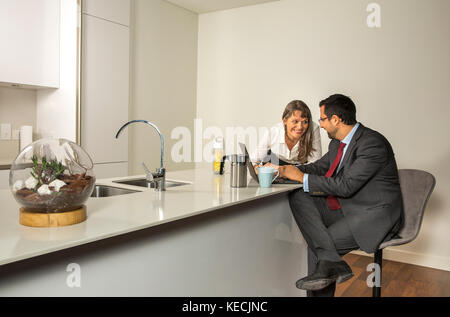 Uomo arabo in formalware lavorando nel suo computer in una cucina del suo appartamento urbano Foto Stock