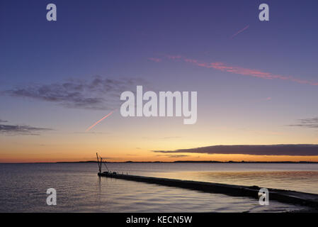 Pier prima del sorgere del sole con la piccola gru stagliano contro il cielo mattutino e rosso brillante vapor trail tettuccio Foto Stock