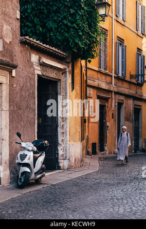 Una suora cammina giù per una strada soleggiata verso un scooter parcheggiati in roma, Italia, dove le suore cattoliche sono una visione comune attraverso la città Foto Stock